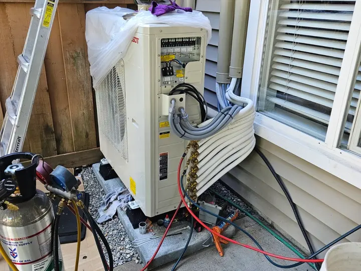TAK technician servicing a Tosot heat pump, with refrigerant gauges and nitrogen connected